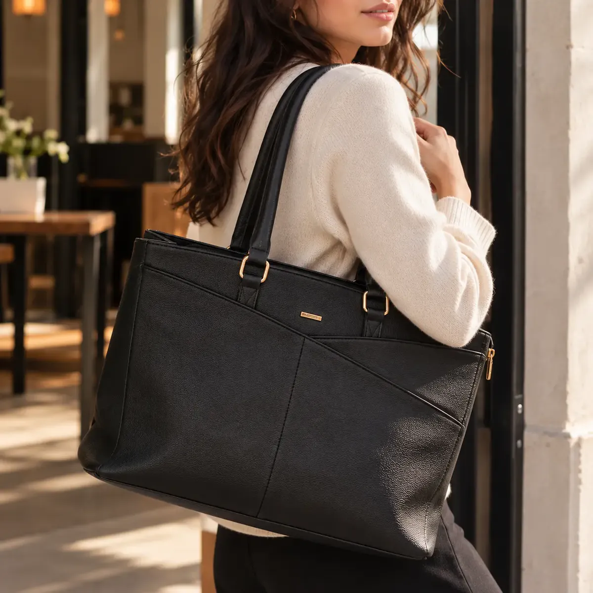Femme en pull crème, le sac Olvia noir à l'épaule devant un café